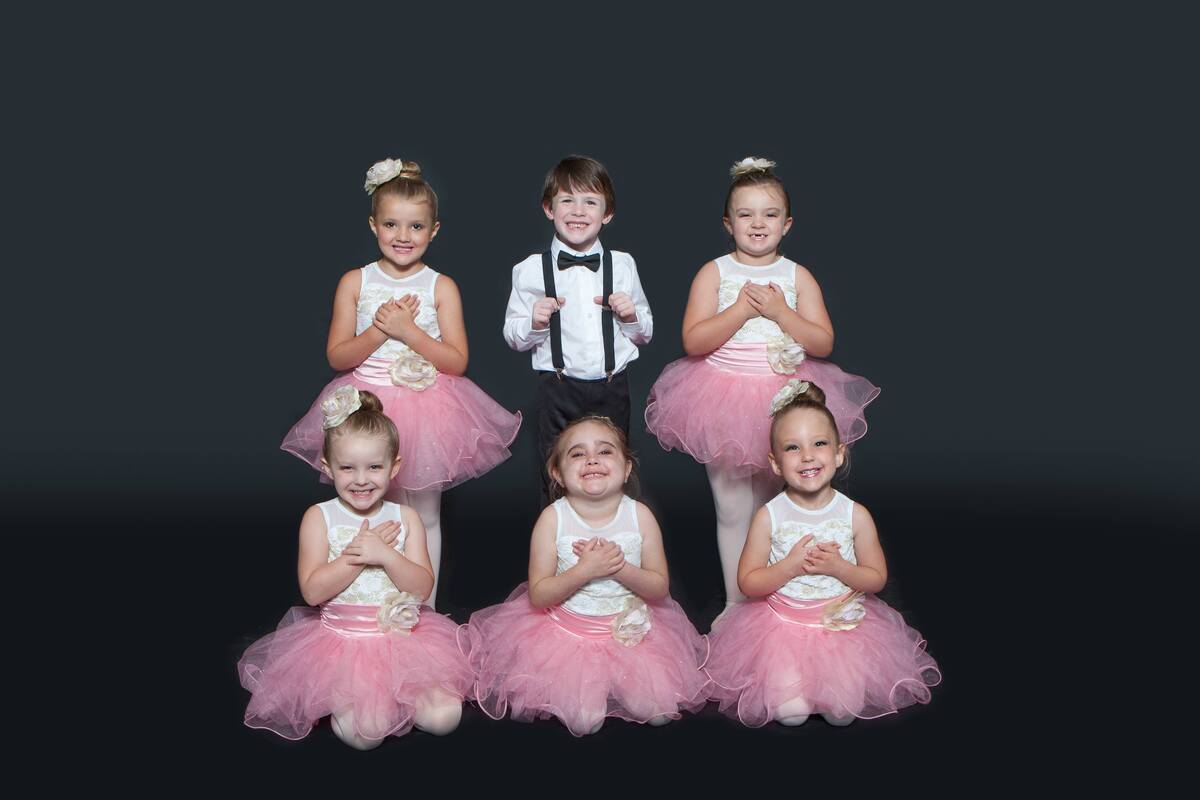 children smiling for picture, girls wearing dance costumes and boy wearing suit